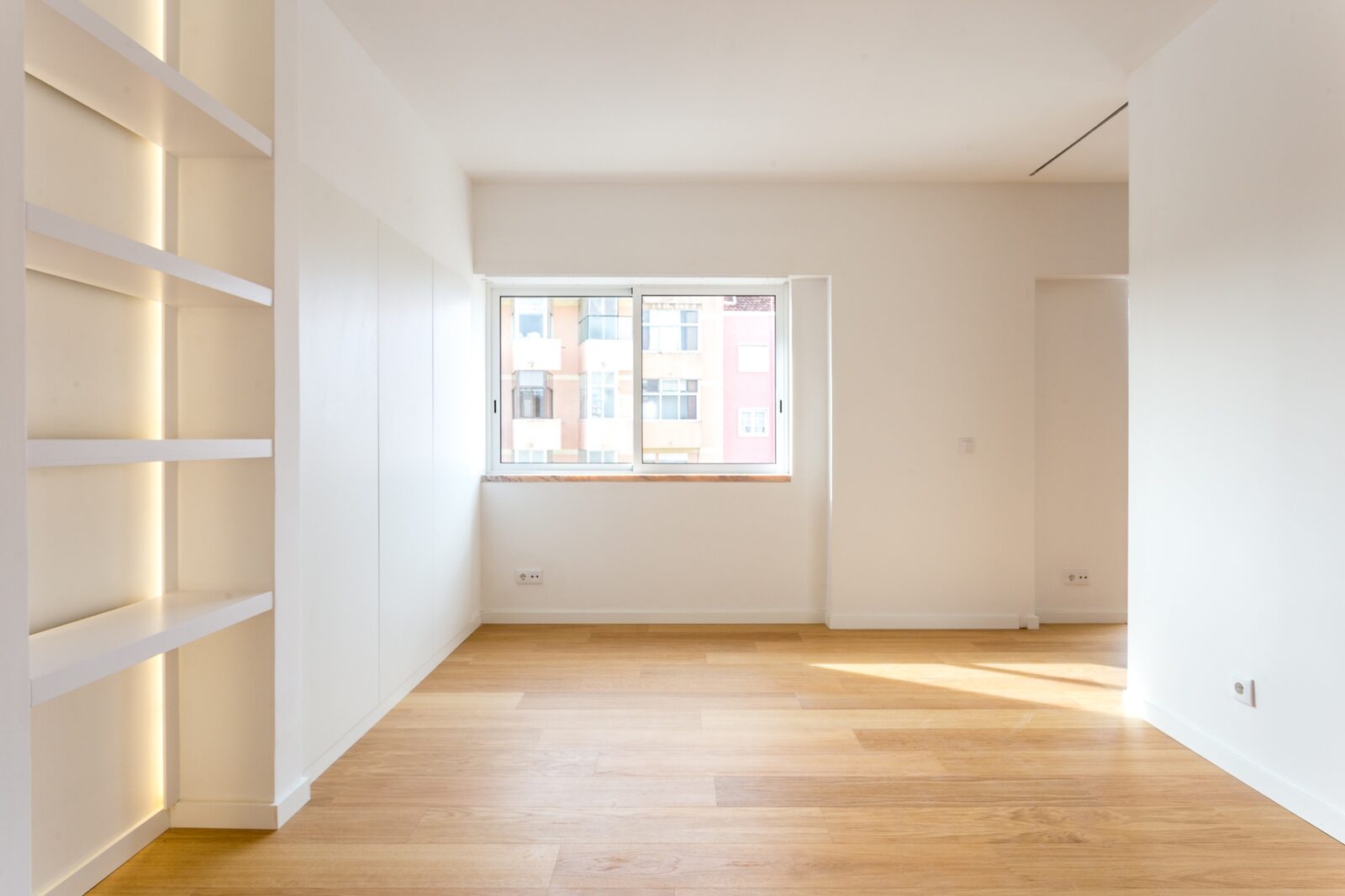 Sala luminosa com estante-nicho iluminada e vista para os prédios da Barceloneta — apartamento remodelado em Barcelona