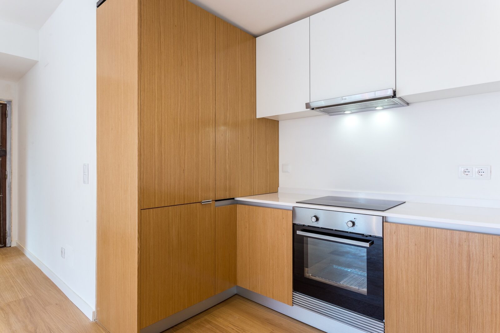 Detalhe da coluna de armários em carvalho com forno encastrado e bancada branca — cozinha na Barceloneta