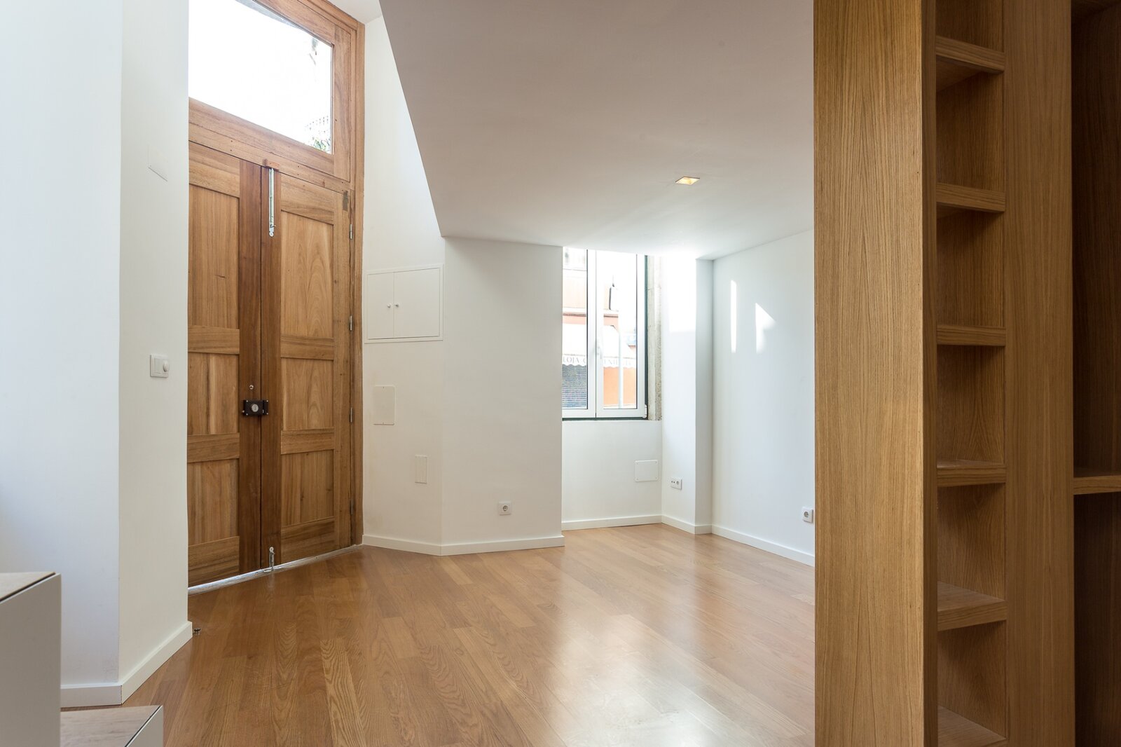 Entrada do loft com estante de carvalho e porta de madeira original ao fundo — Bairro das Colónias