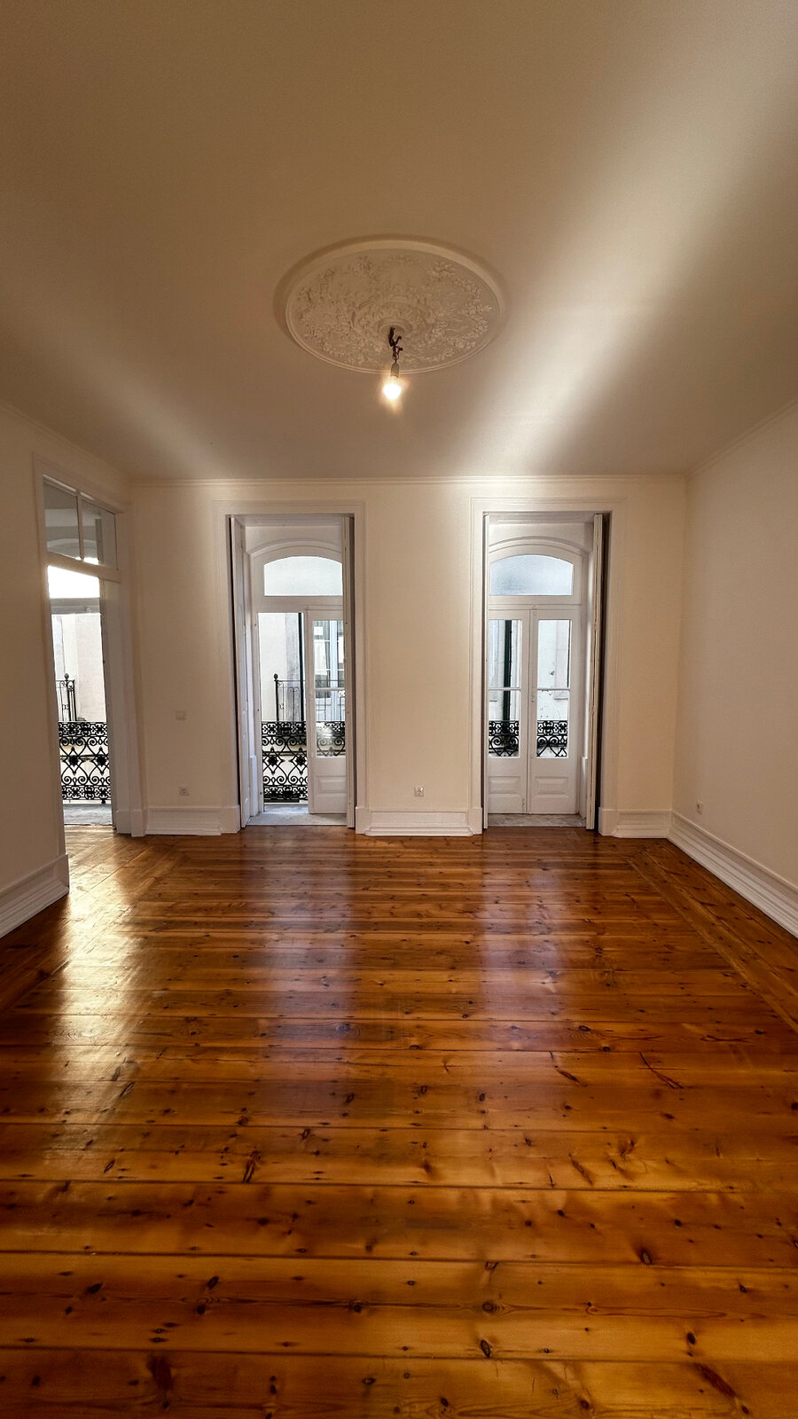 Sala com rosácea de gesso original e portas para varandas com gradeamento em ferro — prédio em Santarém