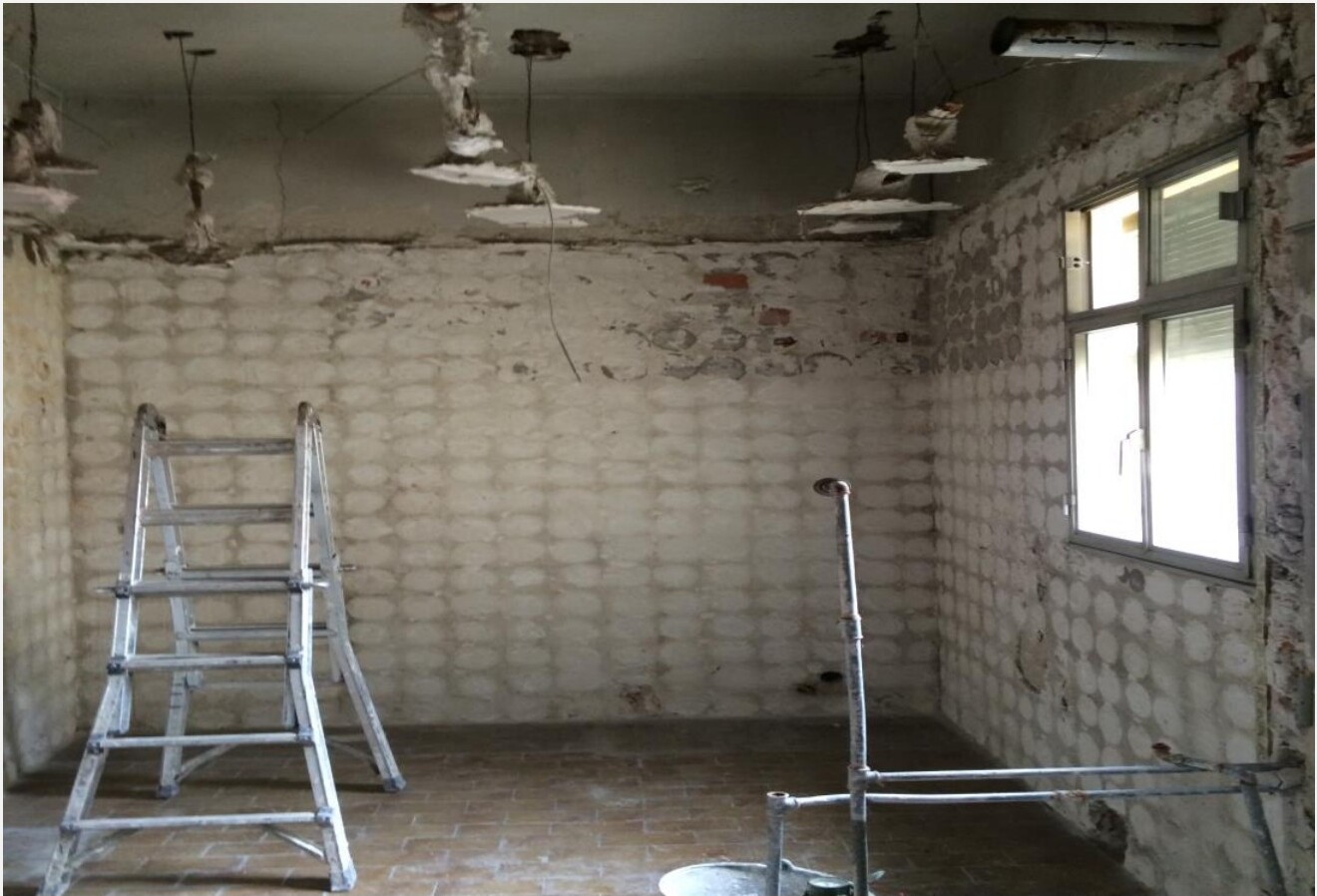 Closet antes da remodelação — paredes de tijolo expostas, escada provisória e tecto danificado, Madrid