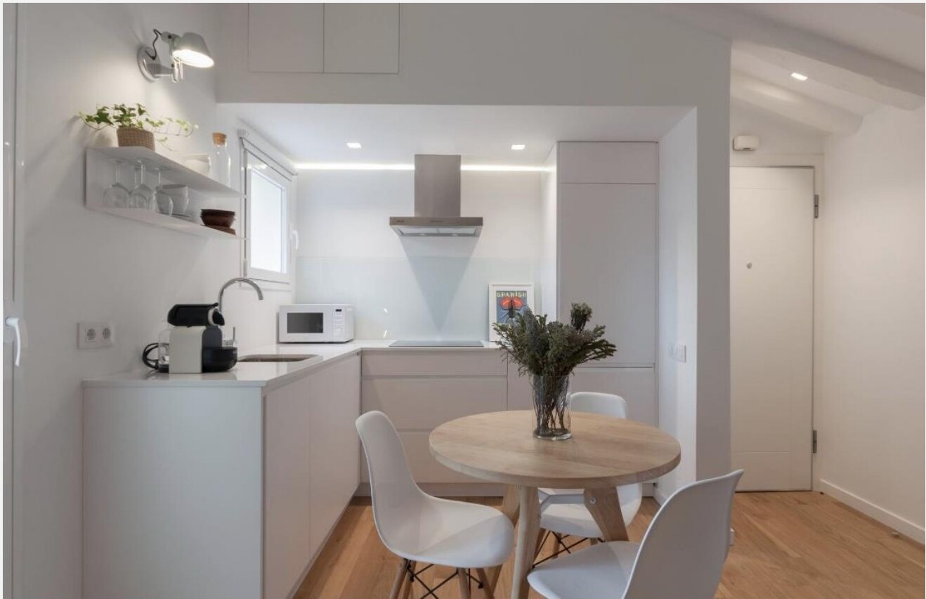 Cozinha branca aberta para sala com mesa de jantar em carvalho — apartamento remodelado em Madrid