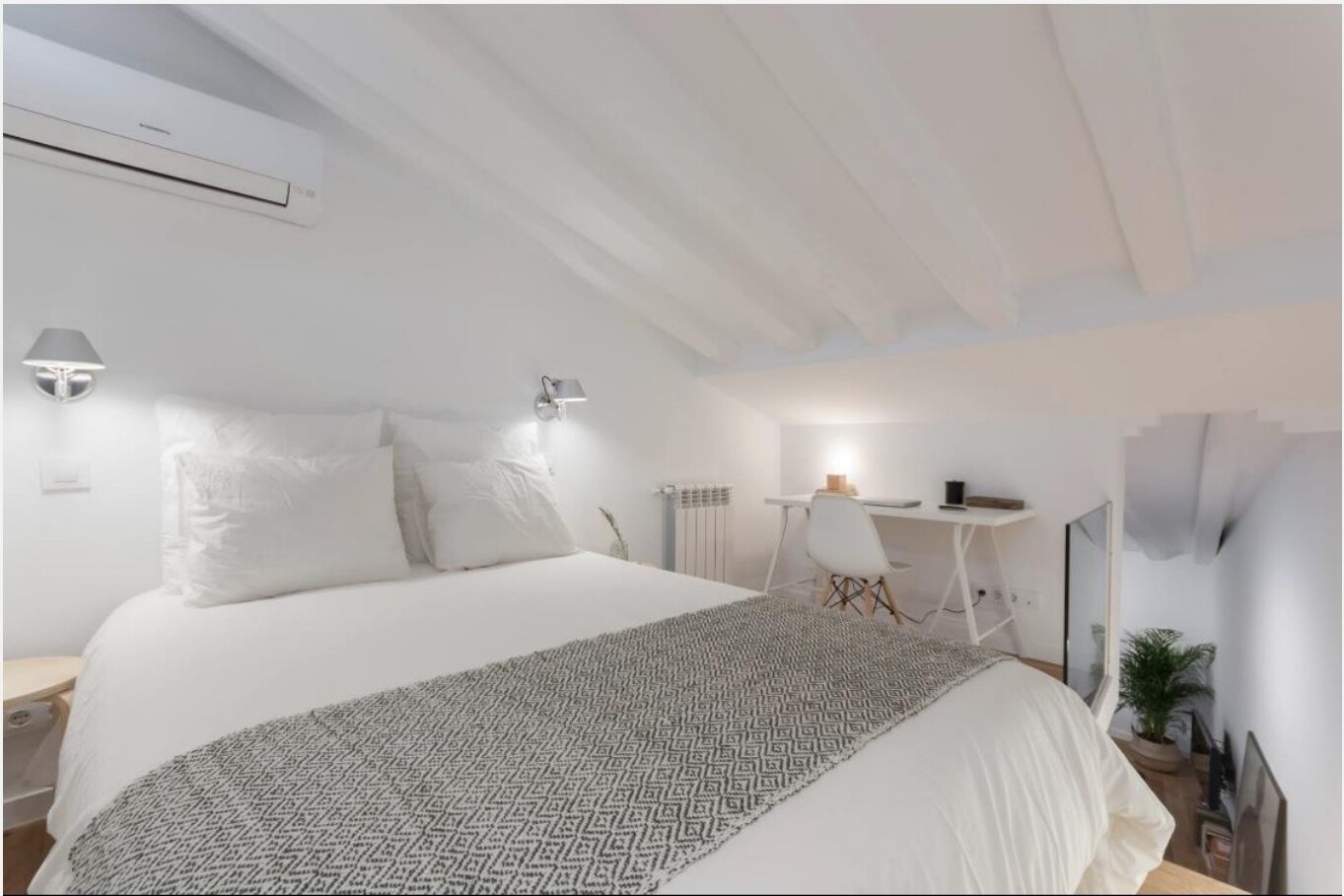 Quarto com cama de casal, paredes brancas, vigas de madeira à vista e zona de trabalho ao fundo — Madrid