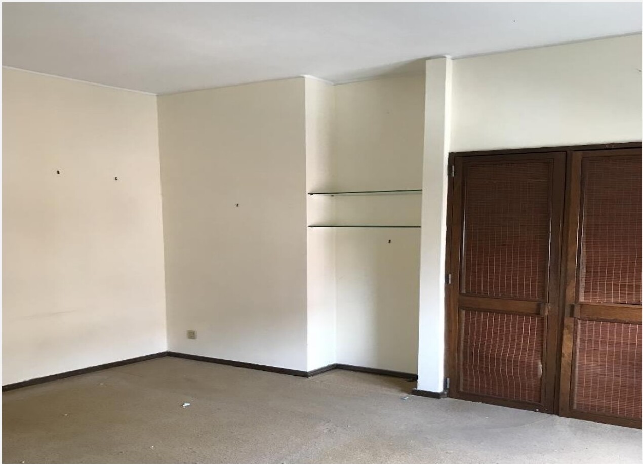 Quarto principal antes — paredes beges, alcatifa, prateleiras em vidro embutidas e portas em madeira escura — Barceloneta
