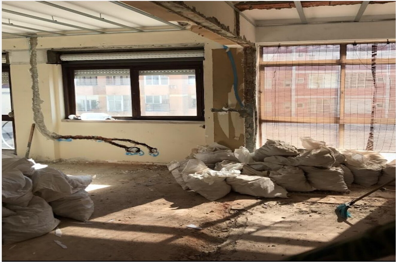 Quarto com vista em obra — paredes em tijolo, instalações eléctricas à vista, sacos de entulho e janela com persiana — Barceloneta