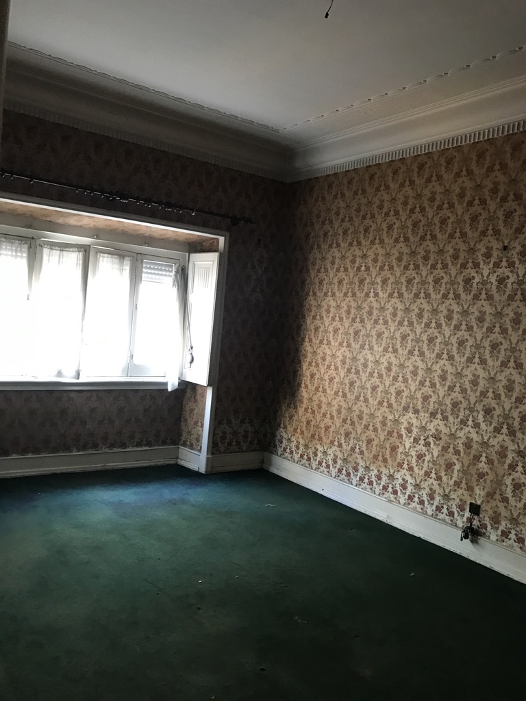 Quarto II antes — papel de parede floral, alcatifa verde-escura e janela com cortinados, Cabo Verde