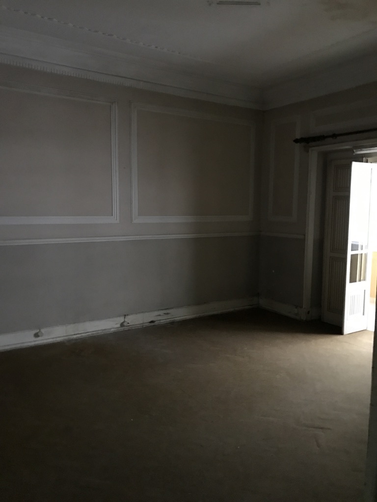 Sala antes — paredes cinzentas com molduras originais, rodapés danificados e portas em madeira pintada, Cabo Verde