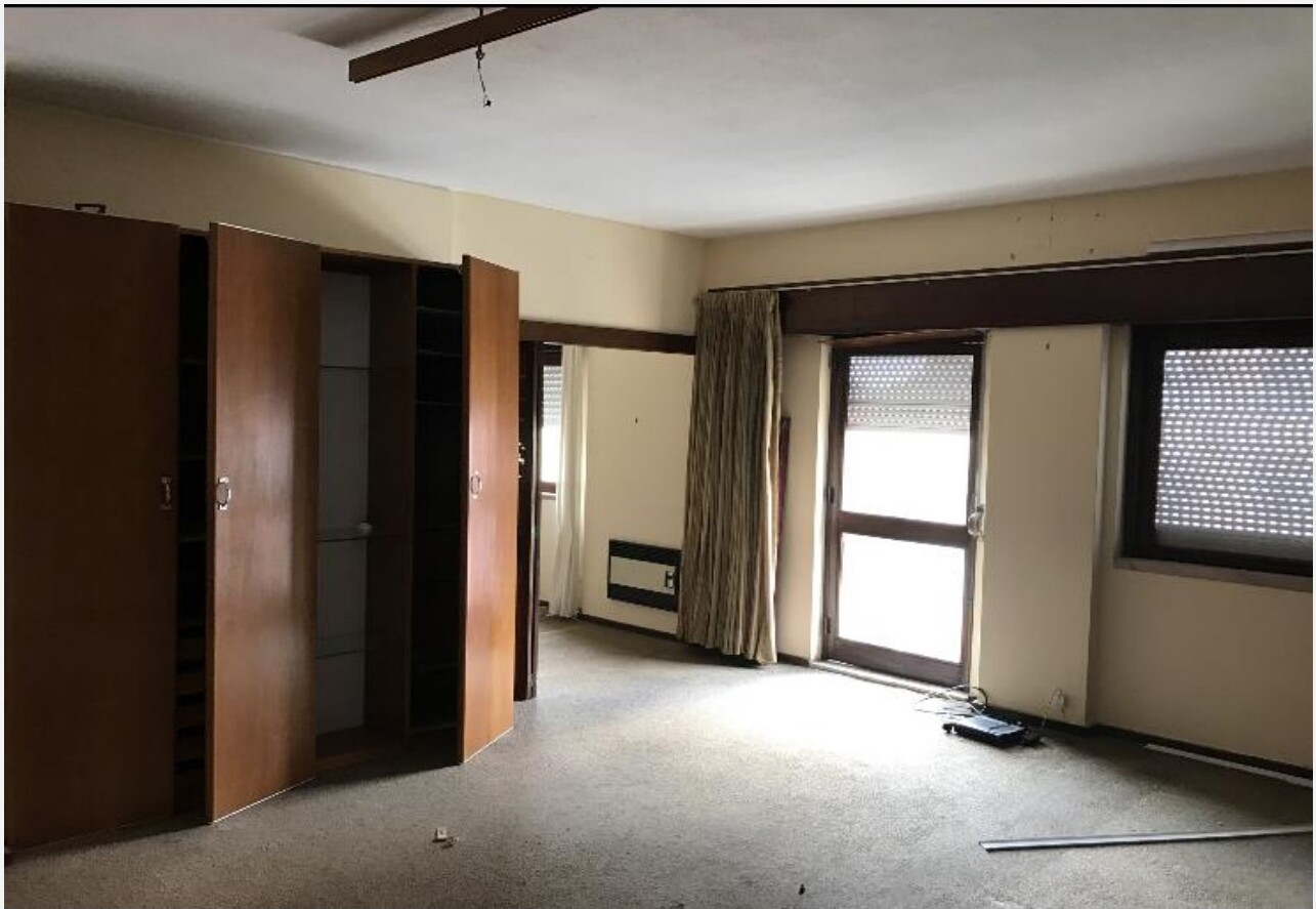 Sala antes da remodelação — paredes beges, alcatifa, viga em madeira escura no tecto e roupeiro antigo aberto — Barceloneta, Barcelona