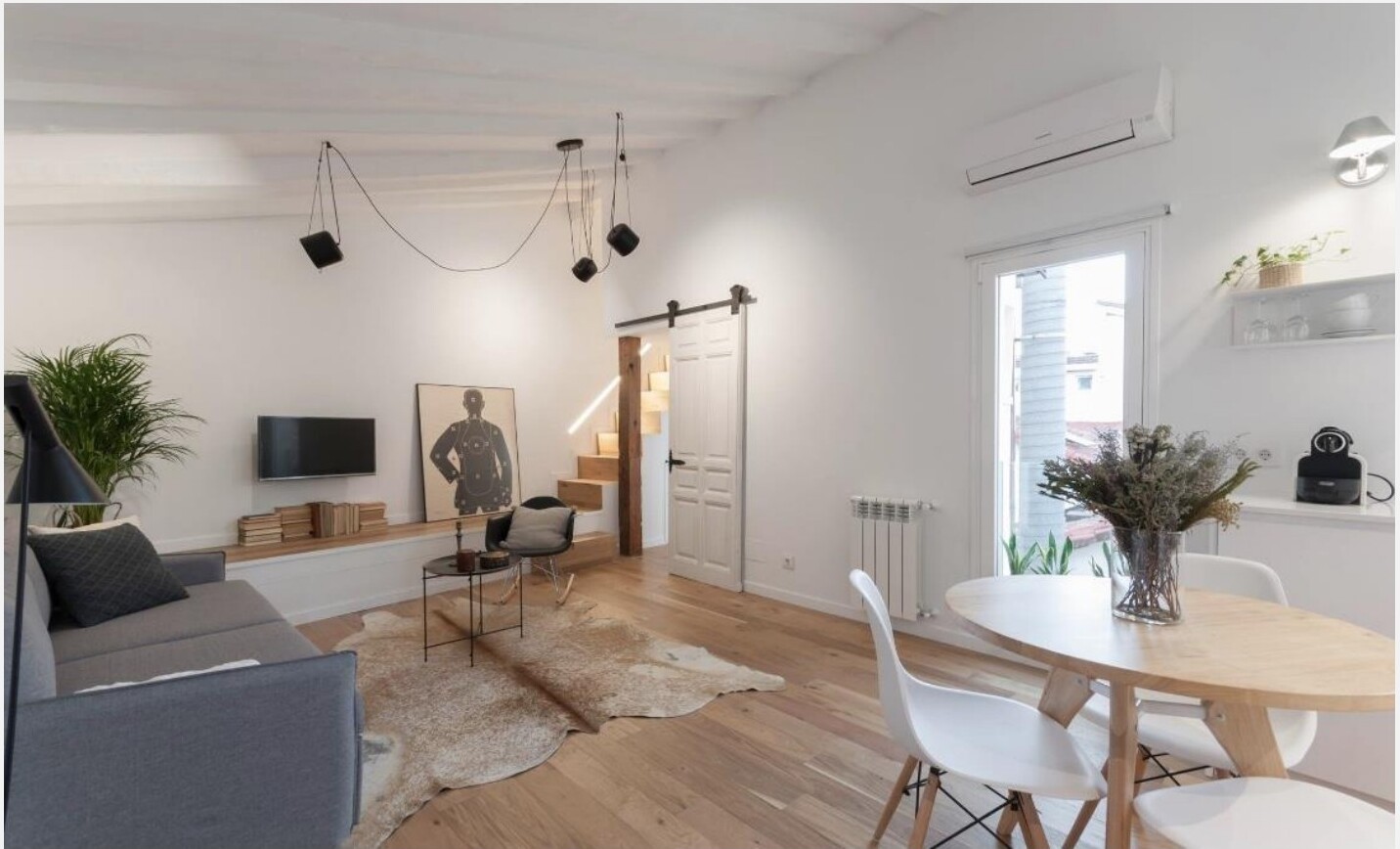 Sala depois da remodelação — tectos brancos, vigas de madeira recuperadas e porta de correr para escada do mezanino, Madrid